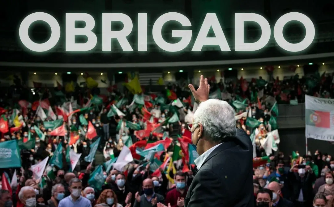 Public speaker addressing a large masked crowd with flags and a banner reading OBRIGADO Public speaker addressing a large masked crowd with flags and a banner reading OBRIGADO