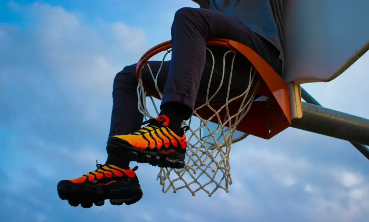 Person sitting on a basketball hoop rim wearing sneakers, in an outdoor setting unrelated to tax residency or the substantial presence test Person sitting on a basketball hoop rim wearing sneakers, in an outdoor setting unrelated to tax residency or the substantial presence test