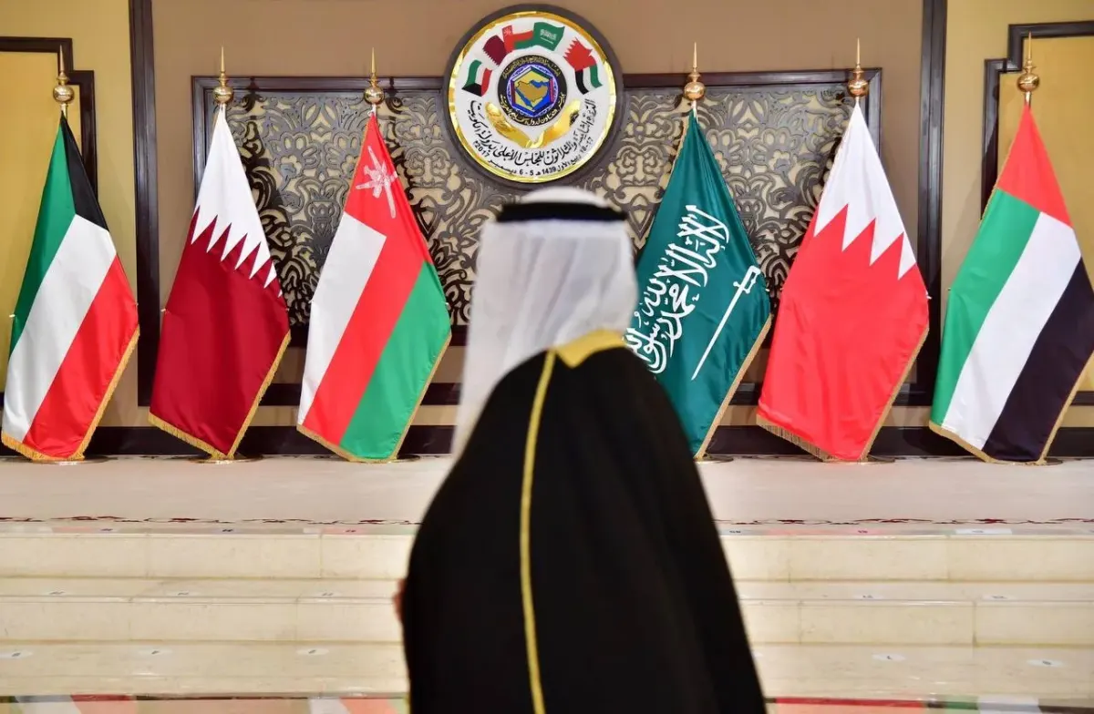 Gulf official in traditional dress standing before GCC country flags in a formal setting Gulf official in traditional dress standing before GCC country flags in a formal setting